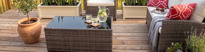 The deck set for the afternoon, woven chairs, a jug of iced water and planters of greenery.