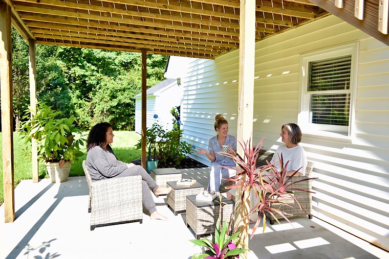 Three guests sitting and talking together on the shaded patio under the deck.