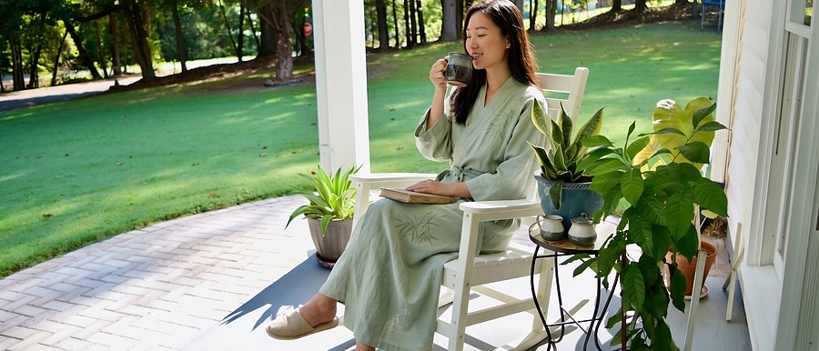 A guest in a robe on the front porch, rocking with a cup of coffee and a book.