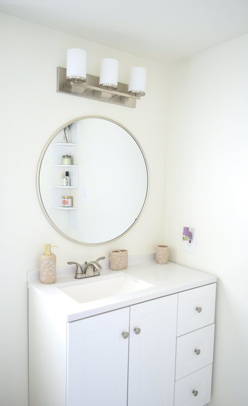 A bathroom vanity with a round mirror and a shelved recess.