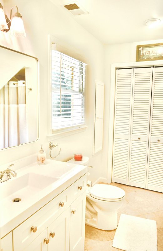 A bathroom with a white vanity, mirror and louvred cupboard doors.