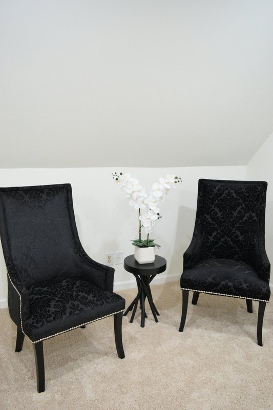 Two black velvet chairs either side of a small table with an orchid on it.