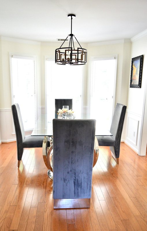 The dining room, a glass table with dark upholstered chairs under a black chandelier.
