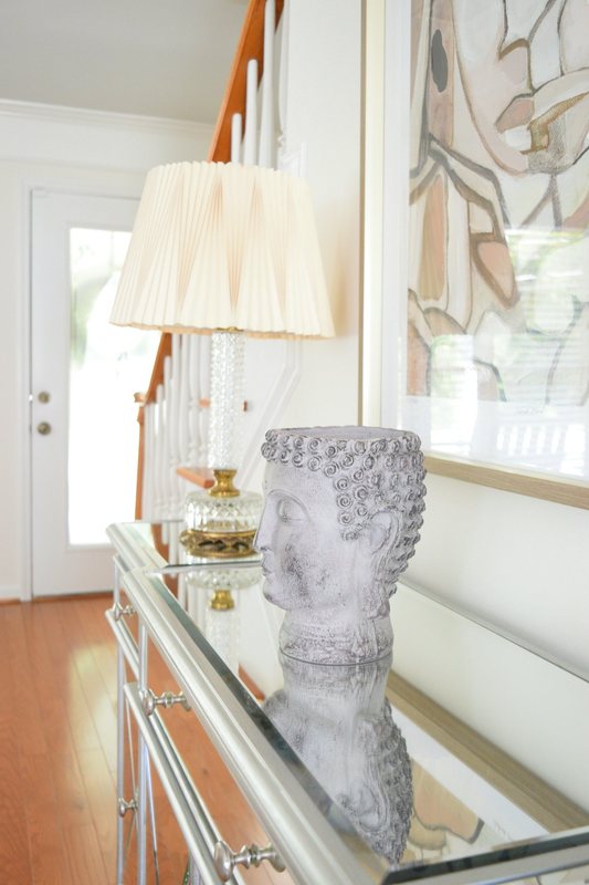 A mirrored console table in the hall with a stone urn and a lamp on it.