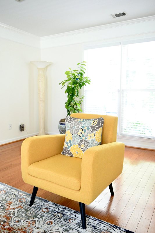 A yellow armchair by the living room window with a plant behind it.