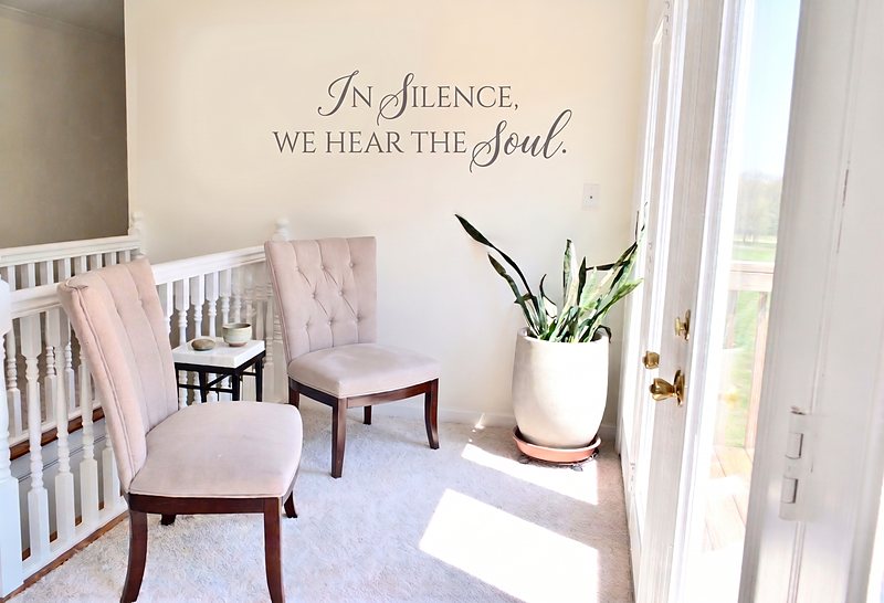 The landing outside the lounge, two chairs and a tall plant beneath the words In Silence, We Hear The Soul.