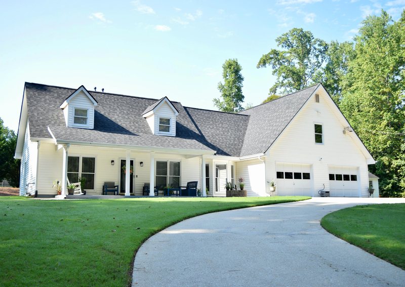 The front of the house from the driveway, a white farmhouse with two dormer windows and a covered porch.