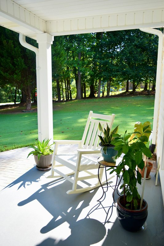 The corner of the porch with a rocking chair and potted plants.