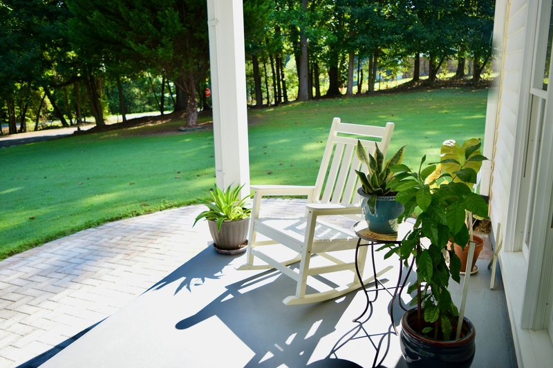 A white rocking chair on the front porch looking out over the lawn and the trees.